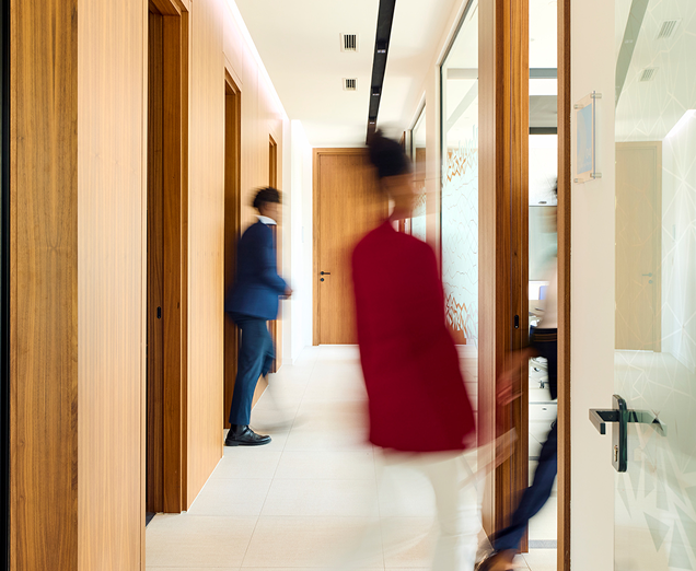 Blurred figures of staff walking briskly through a modern clinical office hallway